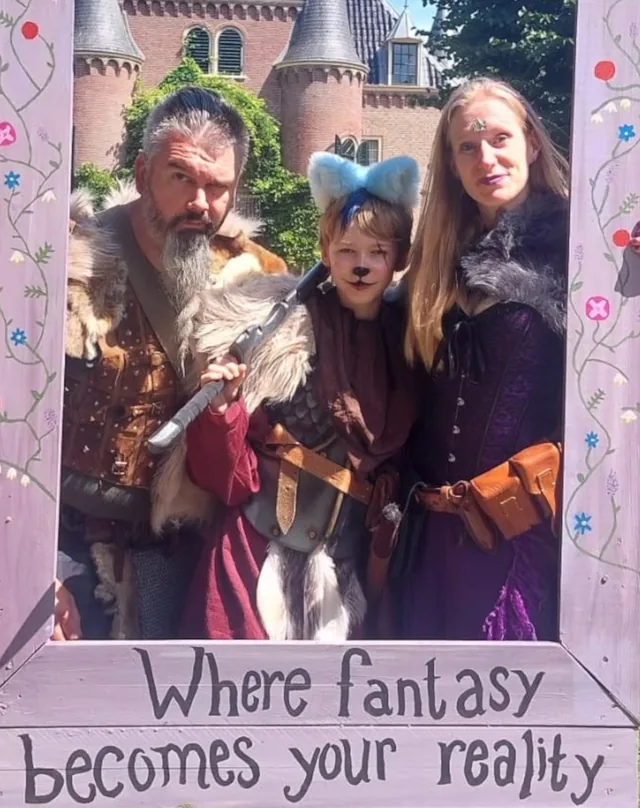 Kim, Haike en Cillian in kostuum op een fantasy-evenement, in een beschilderde fotolijst met de tekst &lsquo;Where fantasy becomes your reality&rsquo;.